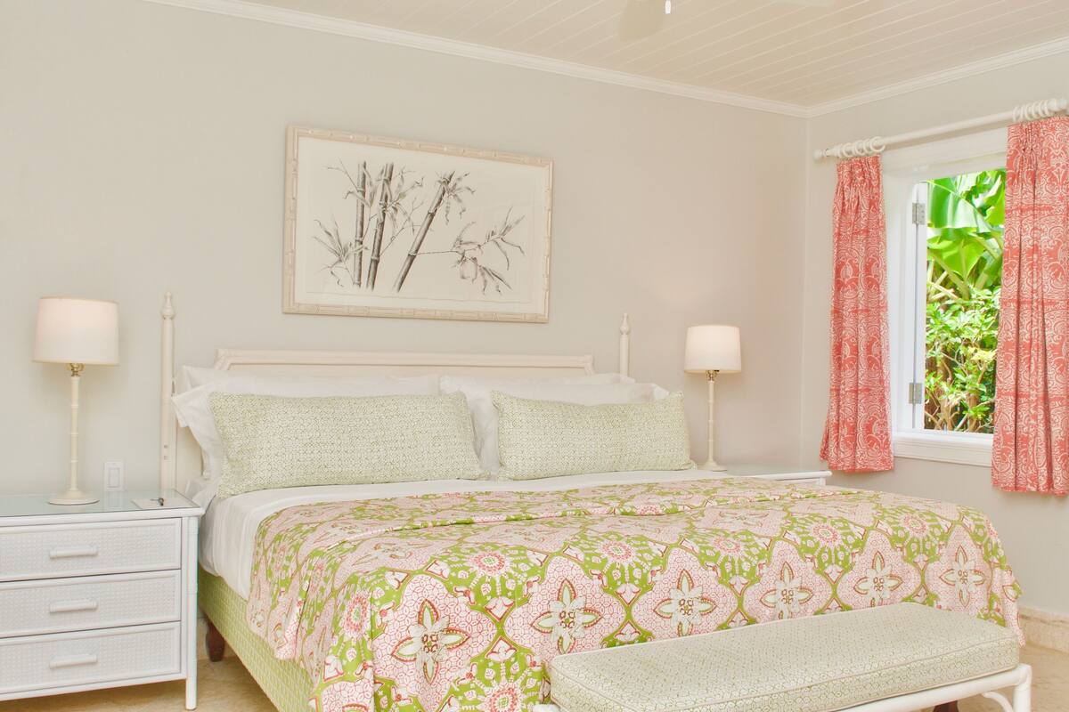 Un dormitorio con cama, mesitas de noche, un banco y una ventana con cortinas.