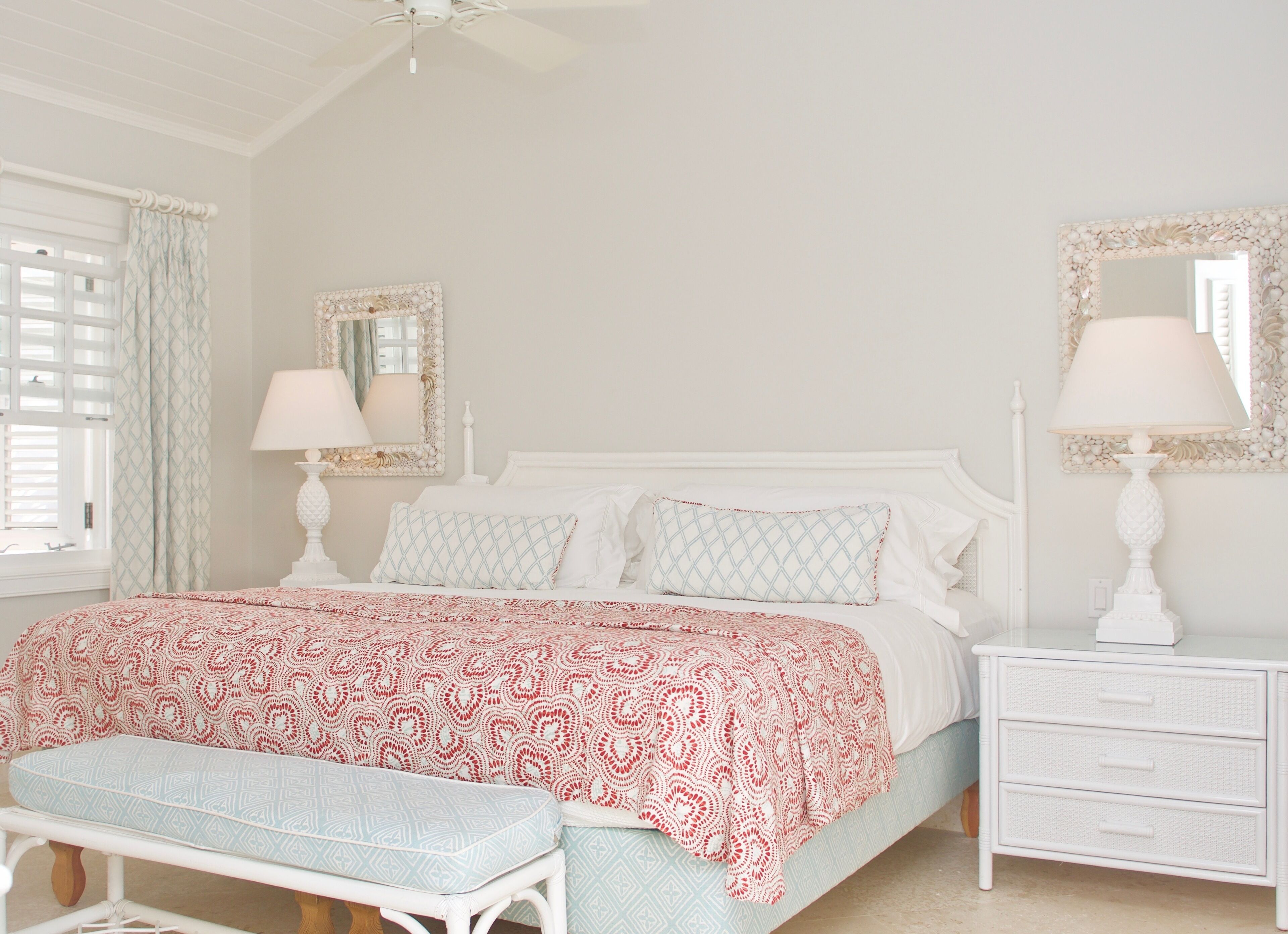 A bedroom with a bed, two bedside tables with lamps, a bench, a window with curtains, and a ceiling fan.