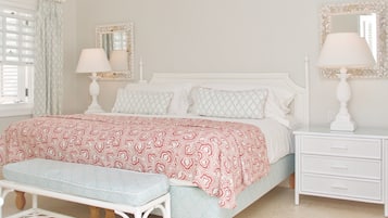 A bedroom with a bed, two bedside tables with lamps, a bench, a window with curtains, and a ceiling fan.
