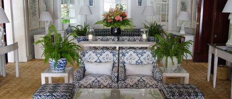 A room with a patterned sofa set, a glass coffee table, and two side tables with lamps and vases.