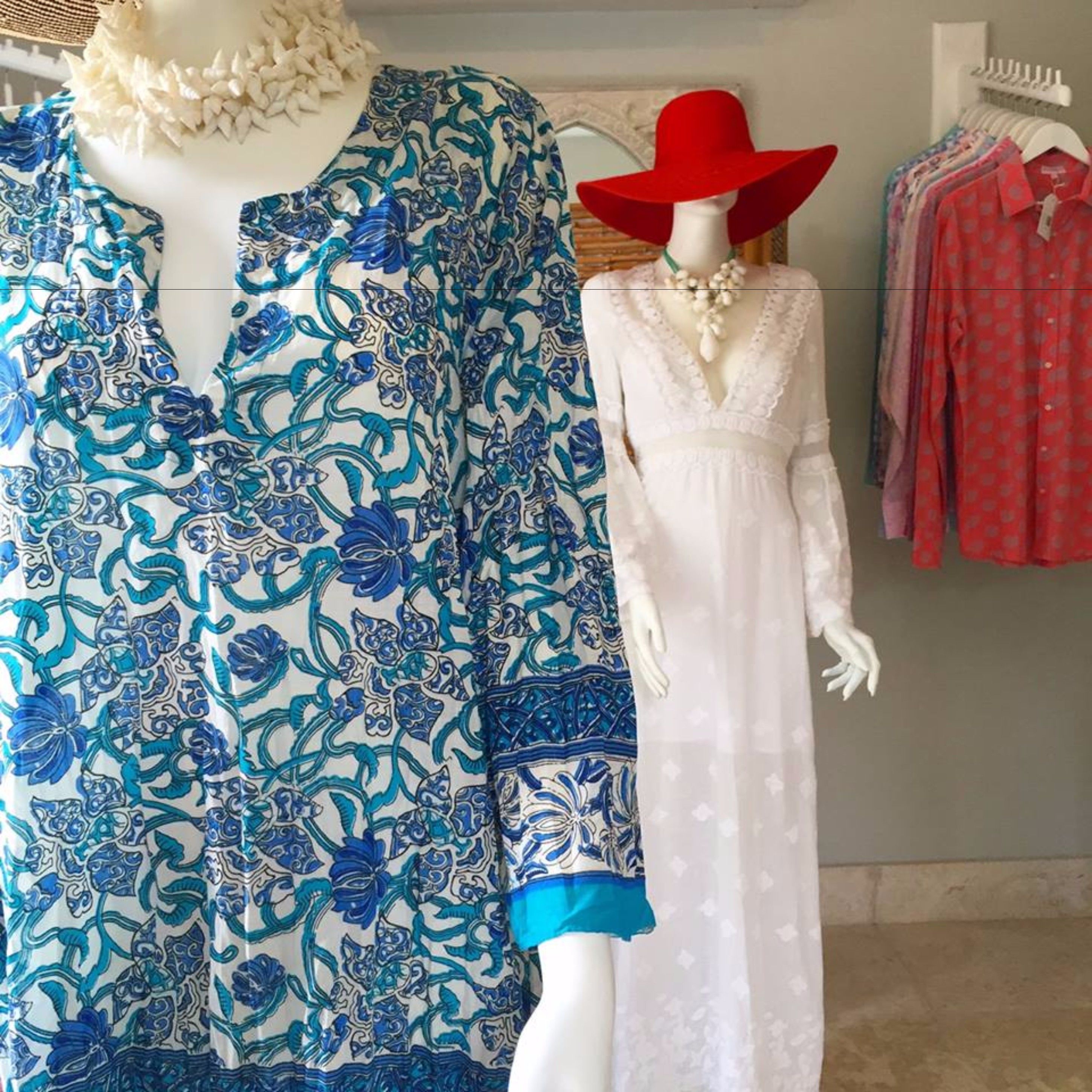 A mannequin dressed in a blue and white patterned dress with a deep V-neckline and a red hat.