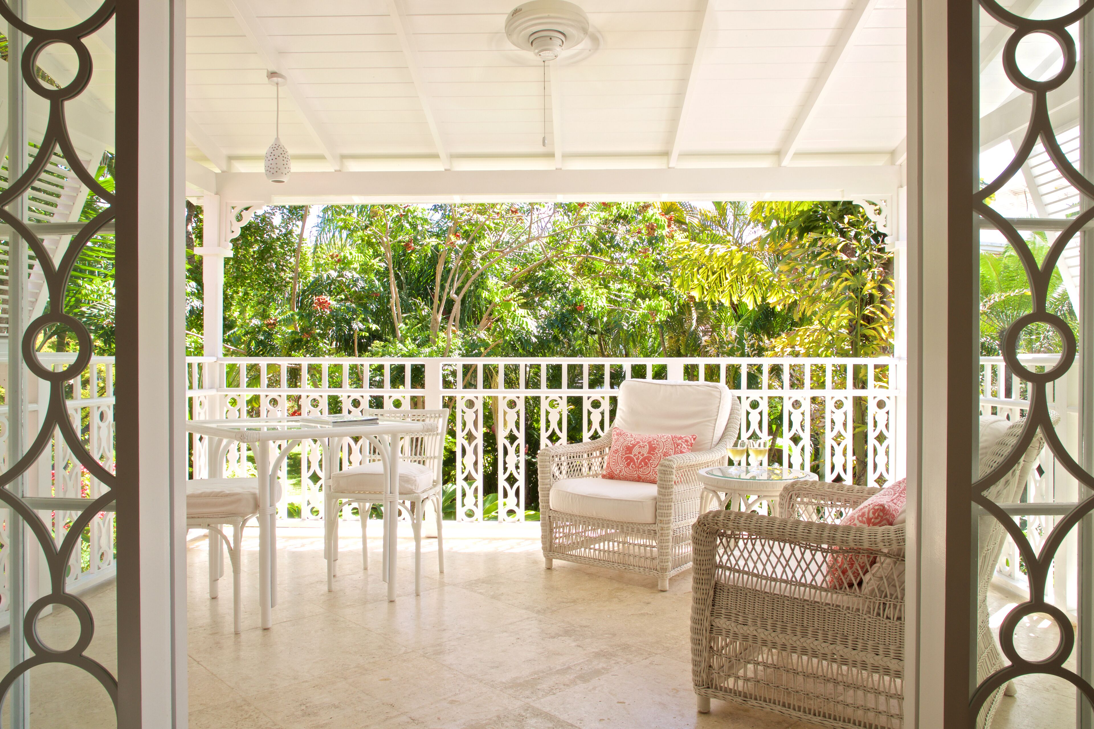 Een overdekt terras met witte wicker meubels en een witte hek.