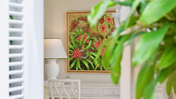 A room with a white desk, a chair, a lamp, and a framed painting of tropical flowers.
