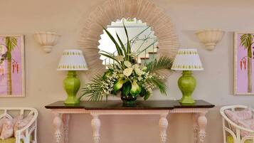 A decorative console table with a mirror, two green lamps, and a floral arrangement.