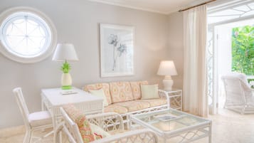 Une pièce avec une fenêtre ronde, un canapé blanc orné de coussins à motifs, une table blanche avec une lampe et un fauteuil en osier.