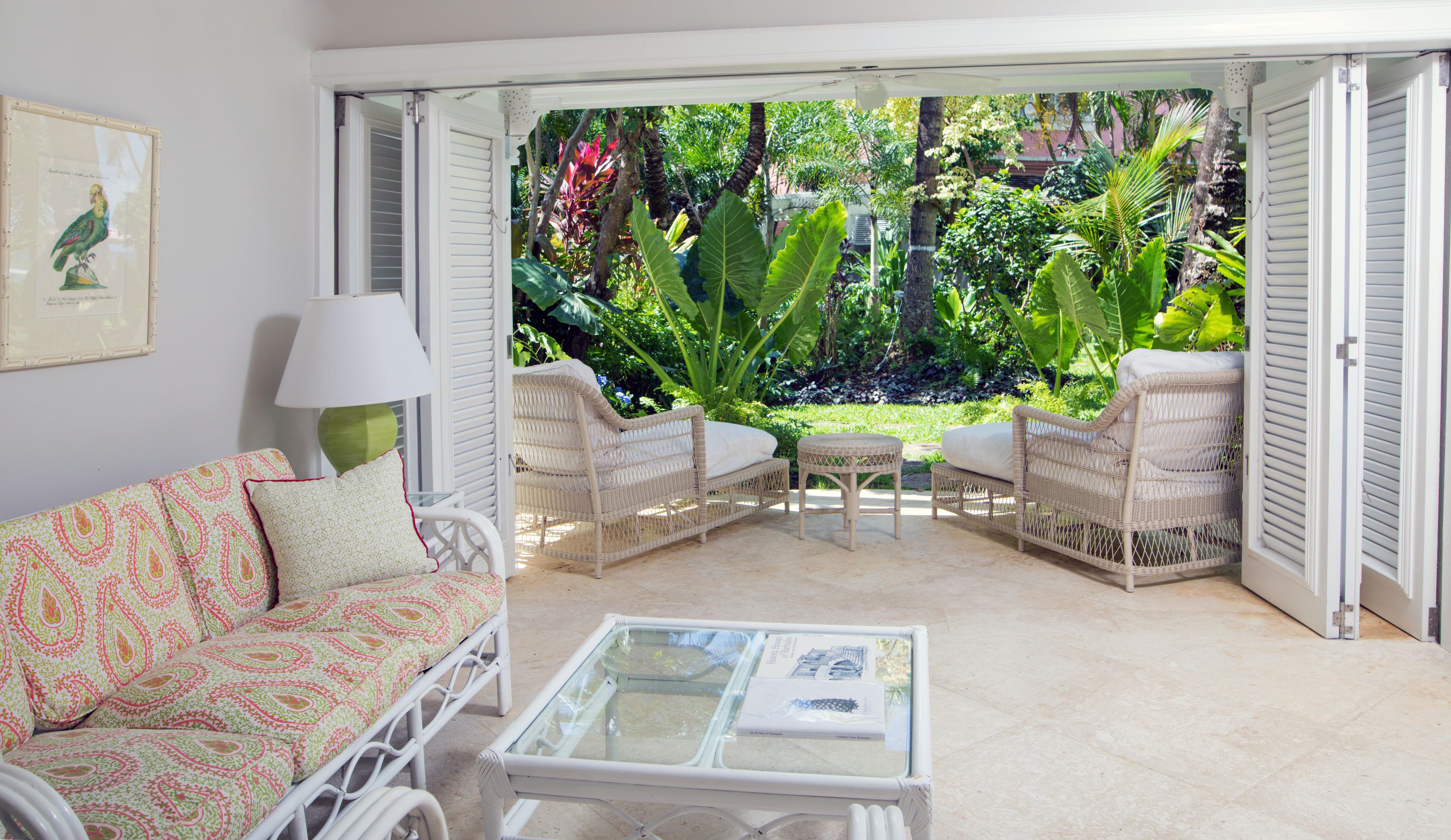 A room with a white wicker sofa, a matching armchair, and a glass coffee table. A framed picture hangs on the wall.