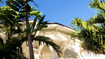 A white building with a balcony and palm trees in the foreground.