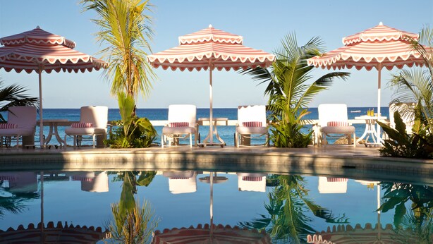 A poolside area with lounge chairs and striped umbrellas, reflecting in the water. - Cobblers Cove - Barbados (Speightstown)