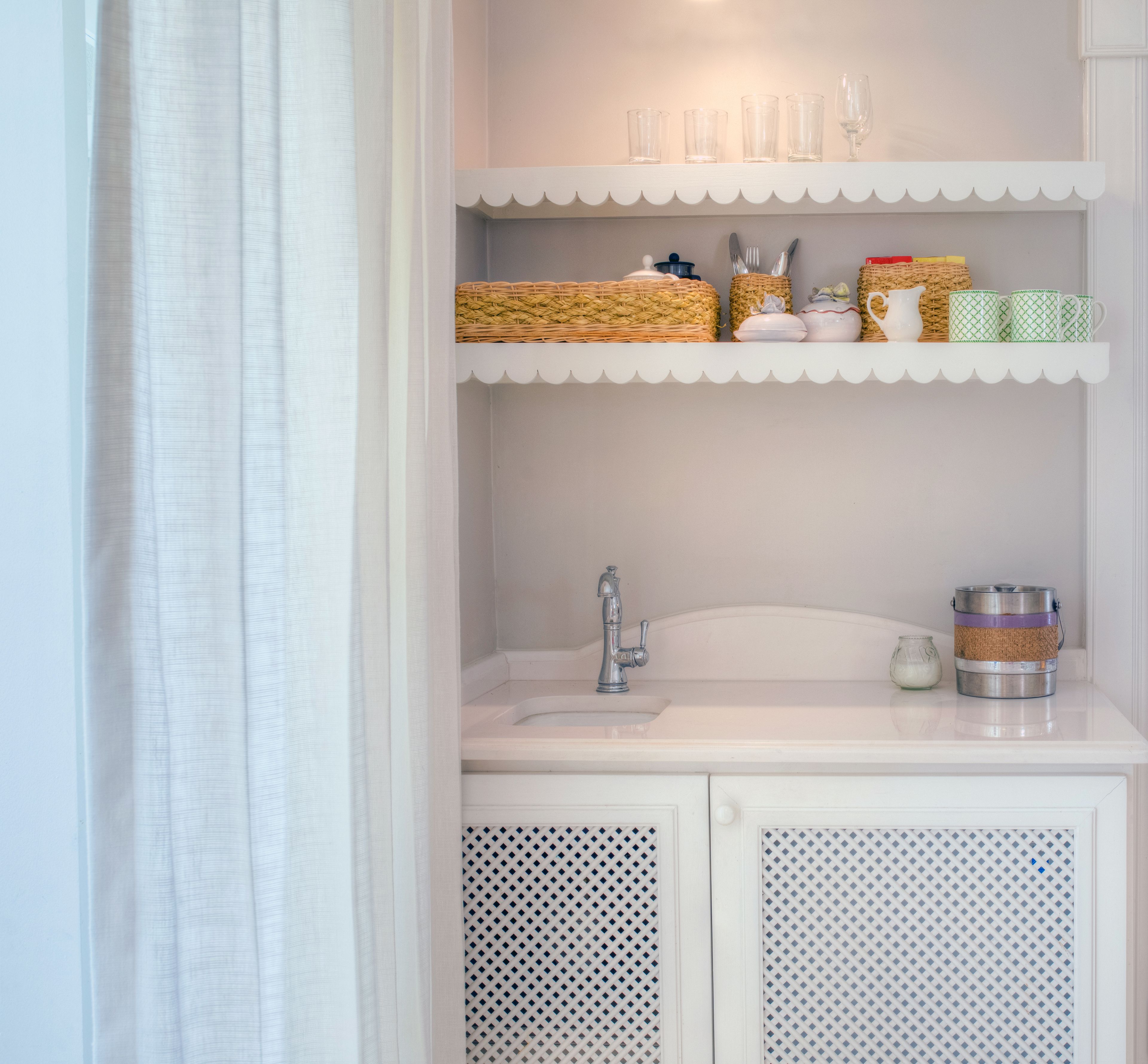 A bathroom with a white sink, a mirror, and shelves above the sink holding various items.