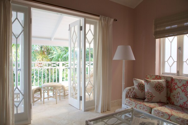 An open door leading to a balcony with wicker furniture and a patterned sofa inside a room with a lamp and a window with a valance. - Cobblers Cove - Barbados (Speightstown)