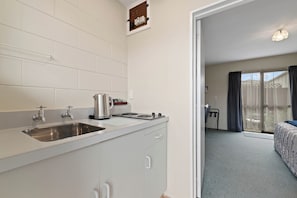 Una kitchenette con un lavamanos de acero inoxidable, una estufa y un hervidor. Hay una puerta que da a un balcón con vistas al exterior.