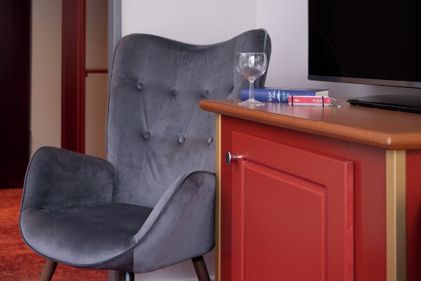 Una butaca tapizada de gris, un armario rojo con encimera de madera y un televisor sobre un mueble.