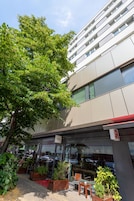 A modern building with a glass entrance, outdoor seating, and a tree in front.