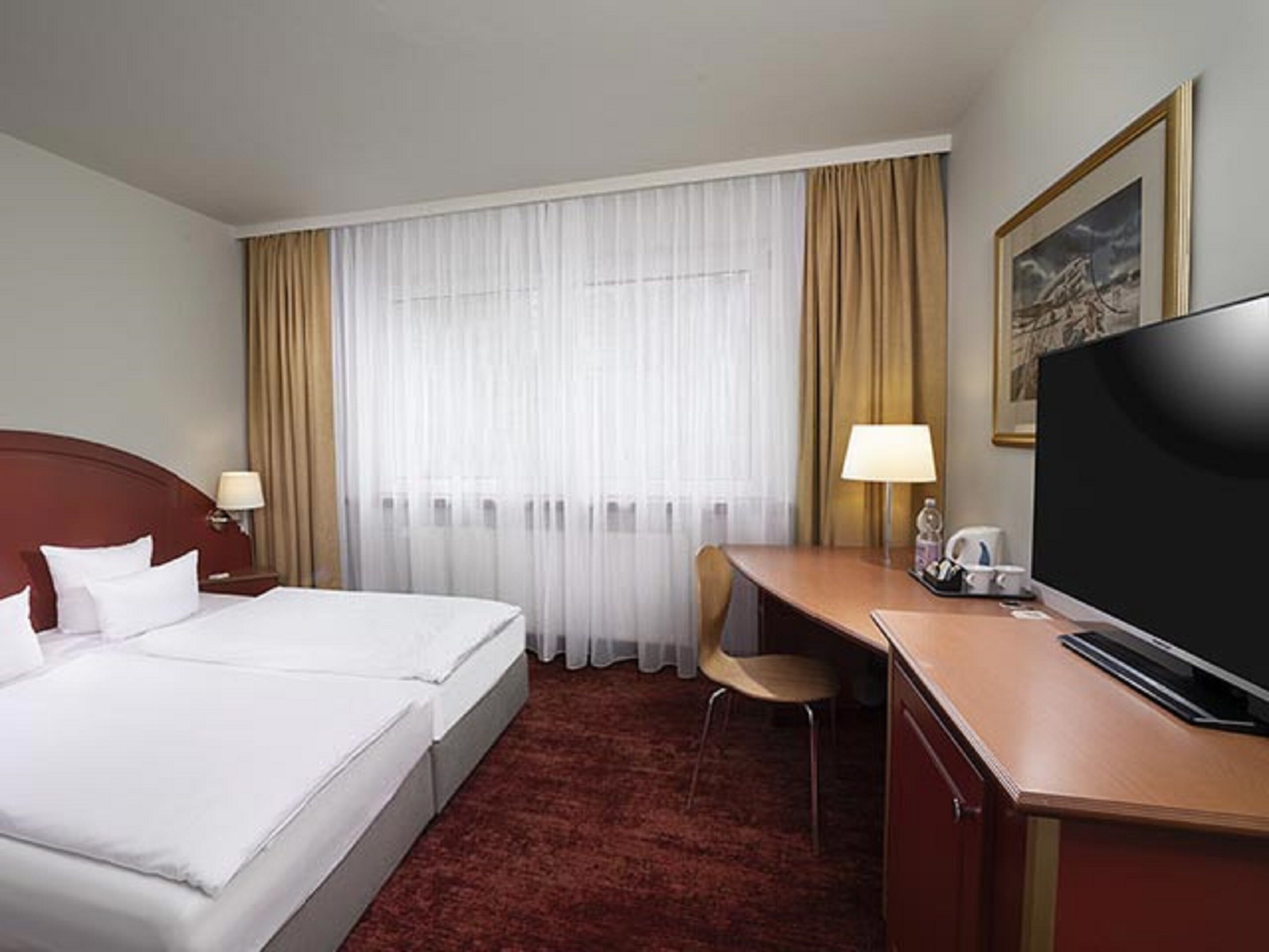 Una habitación de hotel con cama, escritorio, televisión y silla.