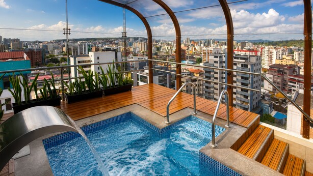 A rooftop pool with a city view, surrounded by plants and wooden deck. - Mercure Alameda Quito (Quito)