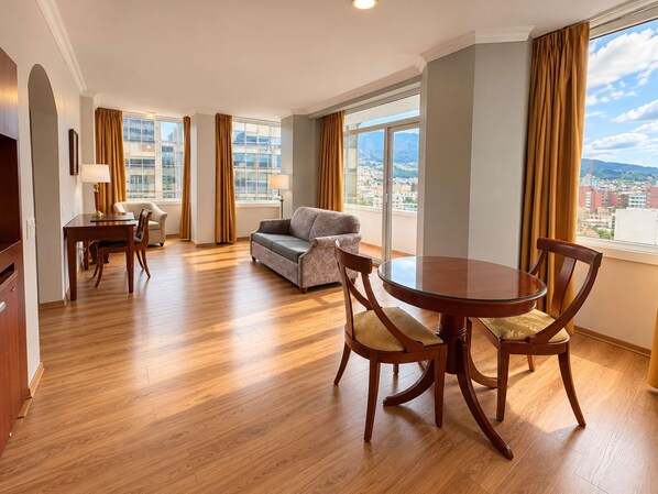 A hotel room with a dining area, a sofa, and a view of the city.