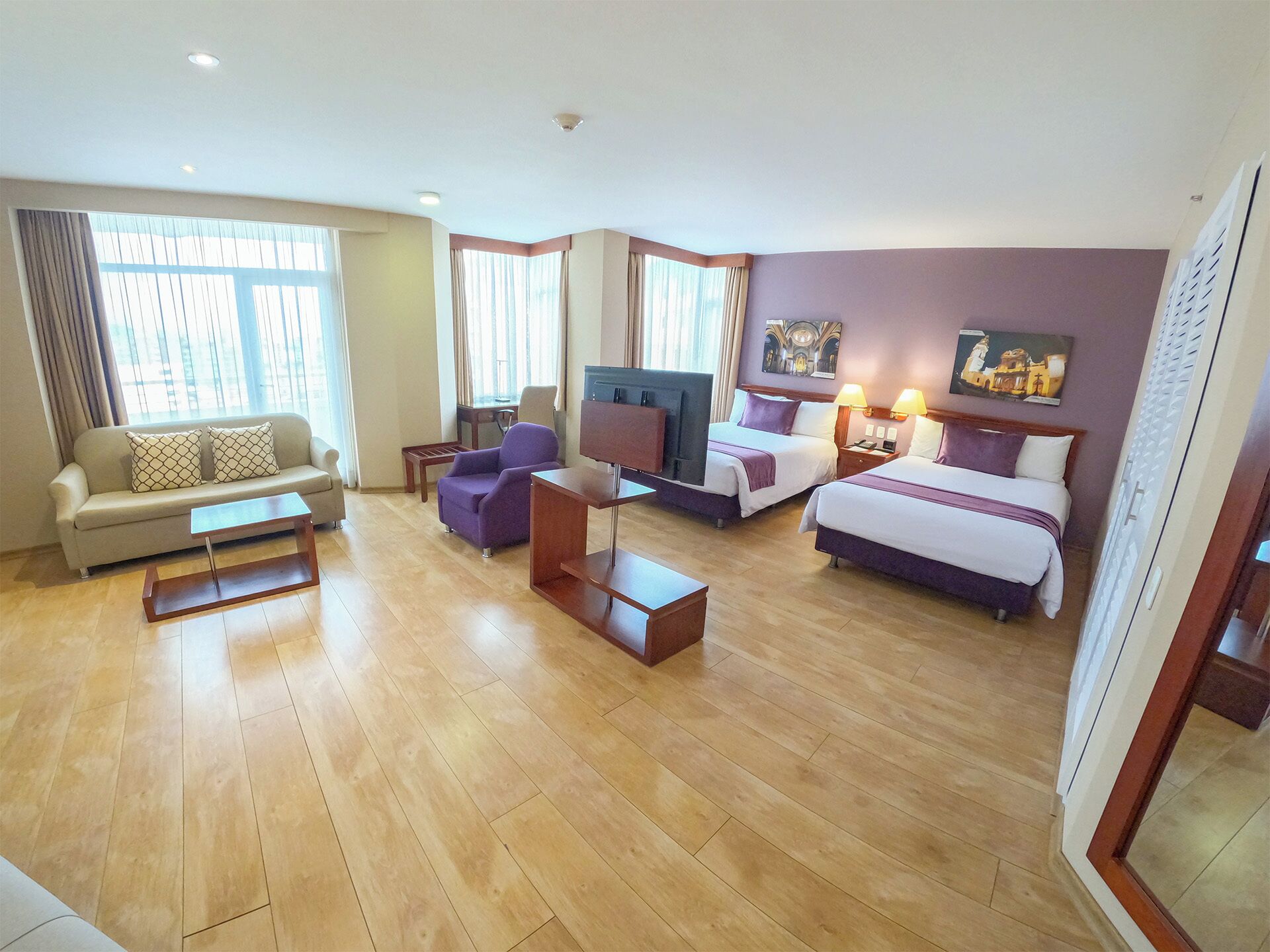 A hotel room with a sofa, armchairs, a TV, a bed, and a desk.