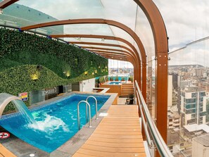 A rooftop pool with a wooden deck, a glass balustrade, and a city view. - Mercure Alameda Quito (Quito)