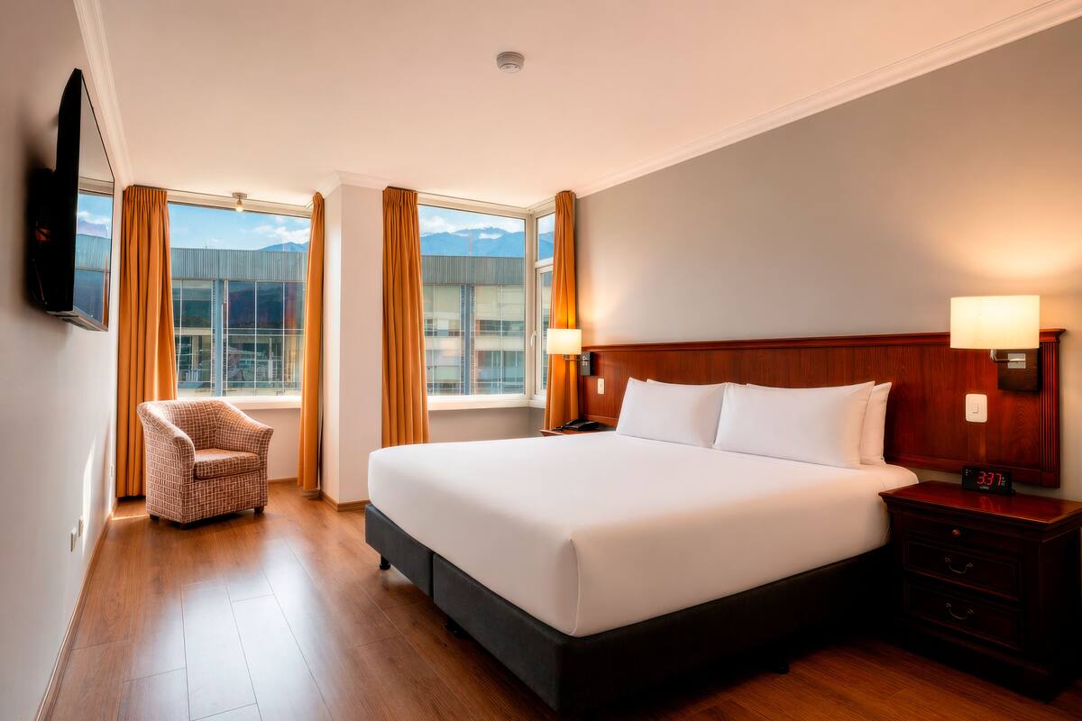 A hotel room with a large bed, a chair, a TV, and a nightstand.