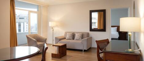 Habitación de hotel con una mesa de comedor redonda, dos sillones, un sofá, una lámpara de pie y un espejo en la pared.