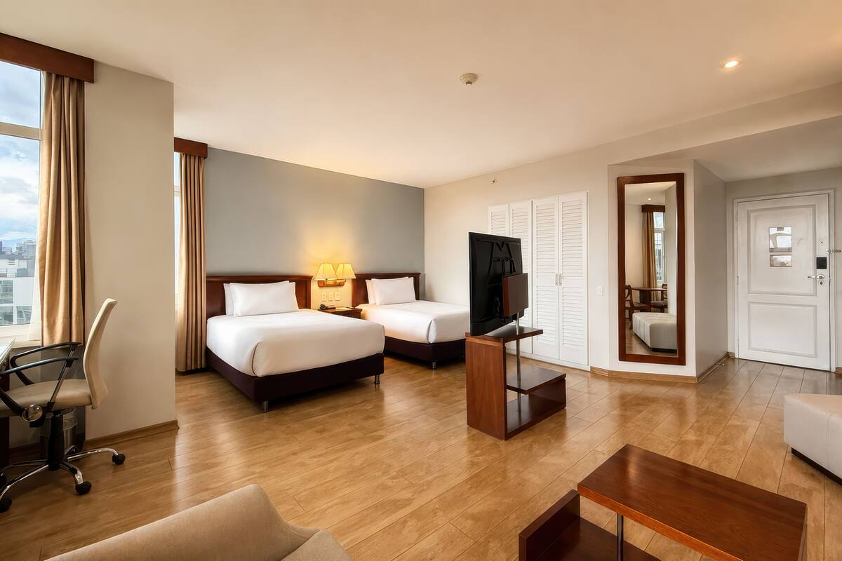 A hotel room with two beds, a TV, a desk, and a chair.