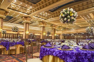 Un salón de banquetes con mesas dispuestas para un evento formal, con detalles ornamentales en el techo y centros de mesa florales.