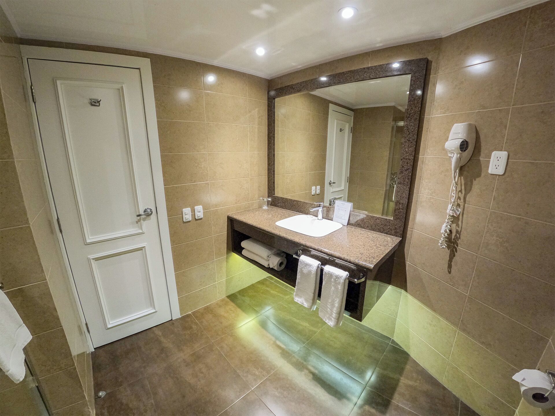 A modern bathroom with a white door, a sink with a mirror above it, a hairdryer, and a toilet.