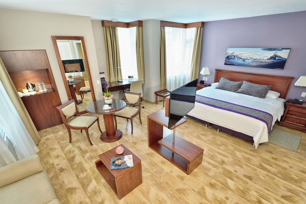 A hotel room with a bed, desk, chair, TV, and a painting on the wall.
