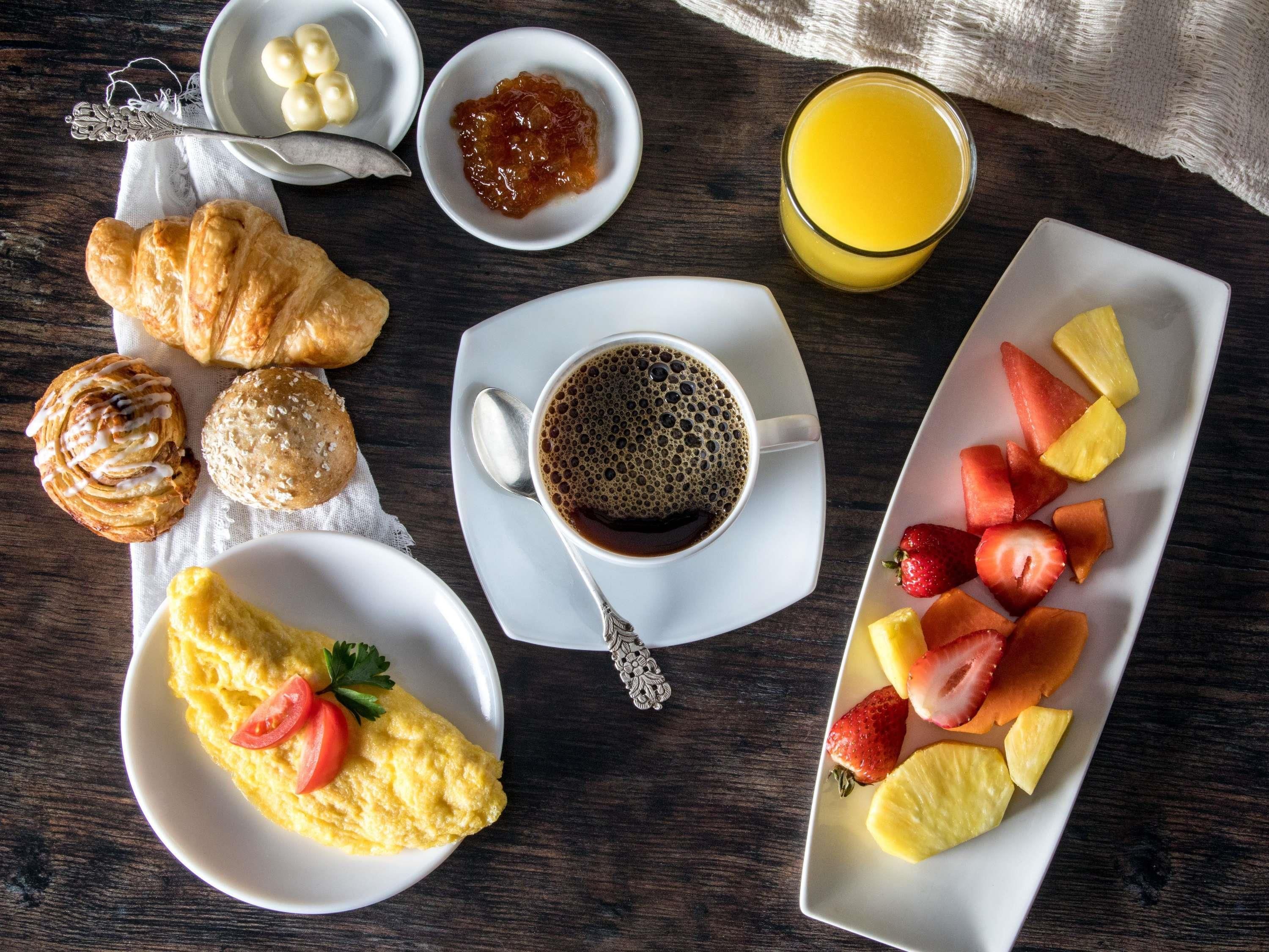 Un desayuno con croissants, una tortilla, café, fruta y mermelada.