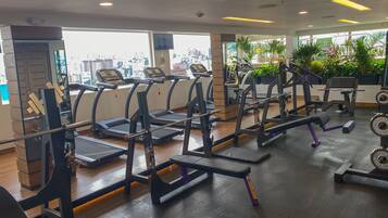Un gimnasio con cintas de correr, máquinas de pesas y vistas a un paisaje urbano a través de amplios ventanales.