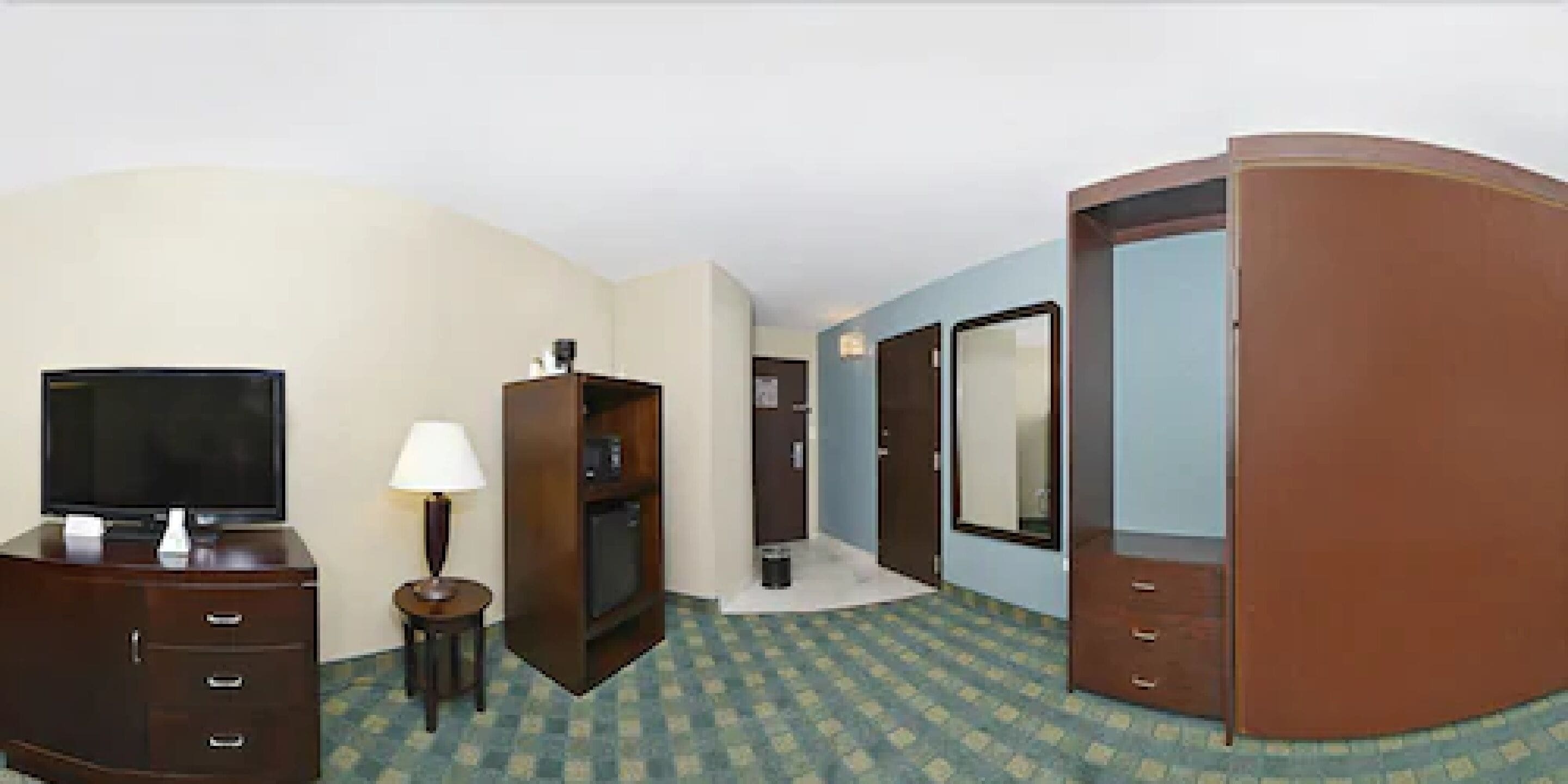 A hotel room with a television, a lamp, a wardrobe, and a mirror.
