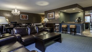 A modern living room with a leather sofa, coffee table, and bar area with stools. - Causeway Bay Hotel (Lansing)