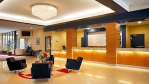 A hotel lobby with a reception desk, seating area, and a chandelier. - Causeway Bay Hotel (Lansing)