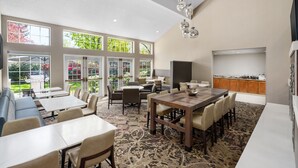 A spacious dining area with multiple tables and chairs, large windows offering views of greenery, and a kitchen area with wooden cabinets. - Residence Inn by Marriott Seattle Northeast-Bothell (Bothell)