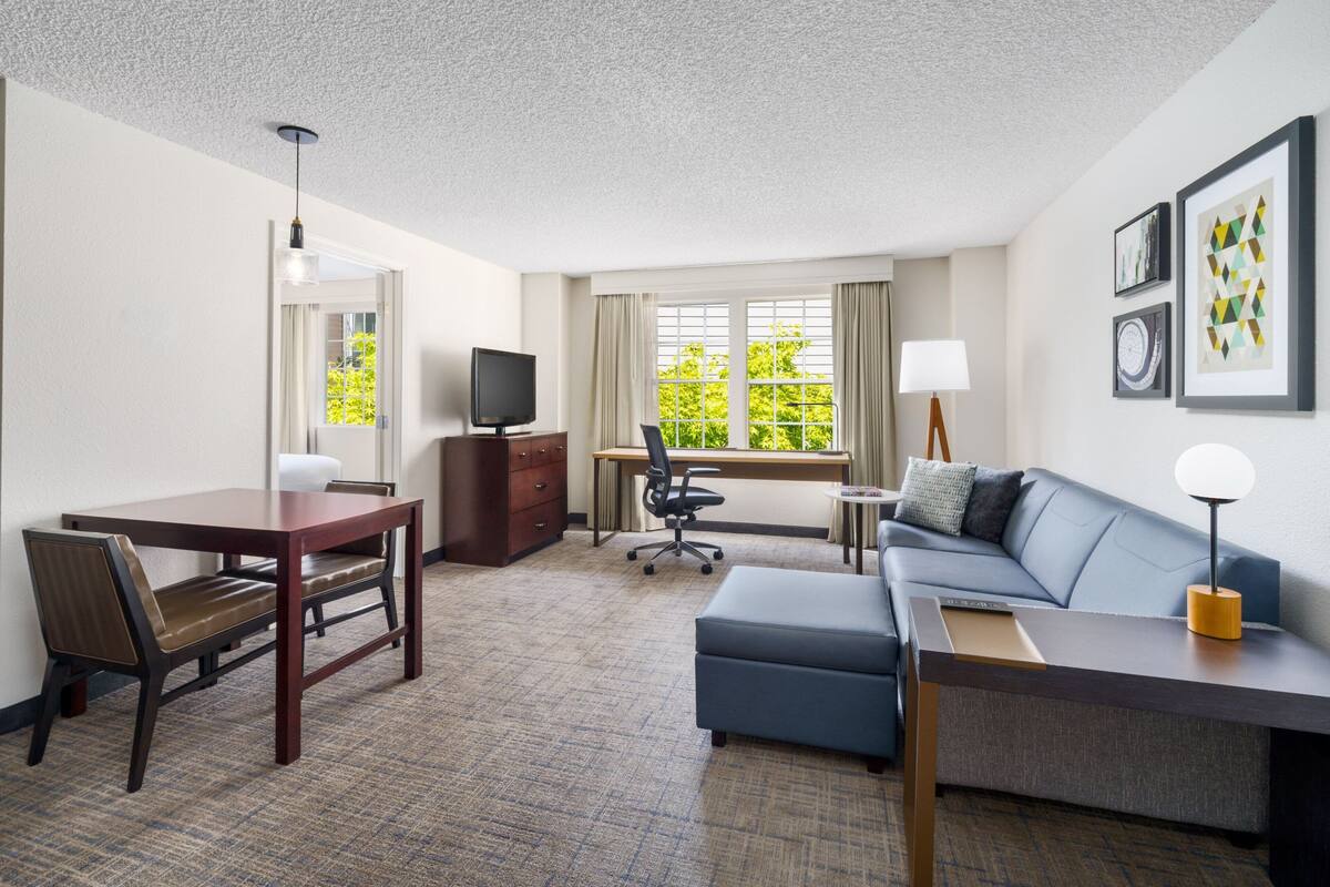 Ein Hotelzimmer mit Esstisch, einer Couch, einem Schreibtisch und einem Fernseher.