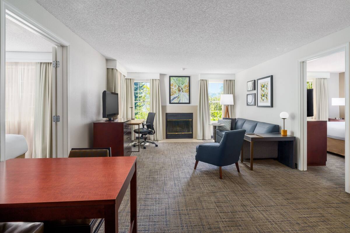 Ein Hotelzimmer mit einem Holztisch, einem blauen Sessel, einem Sofa, einem Fernseher und einem Kamin.