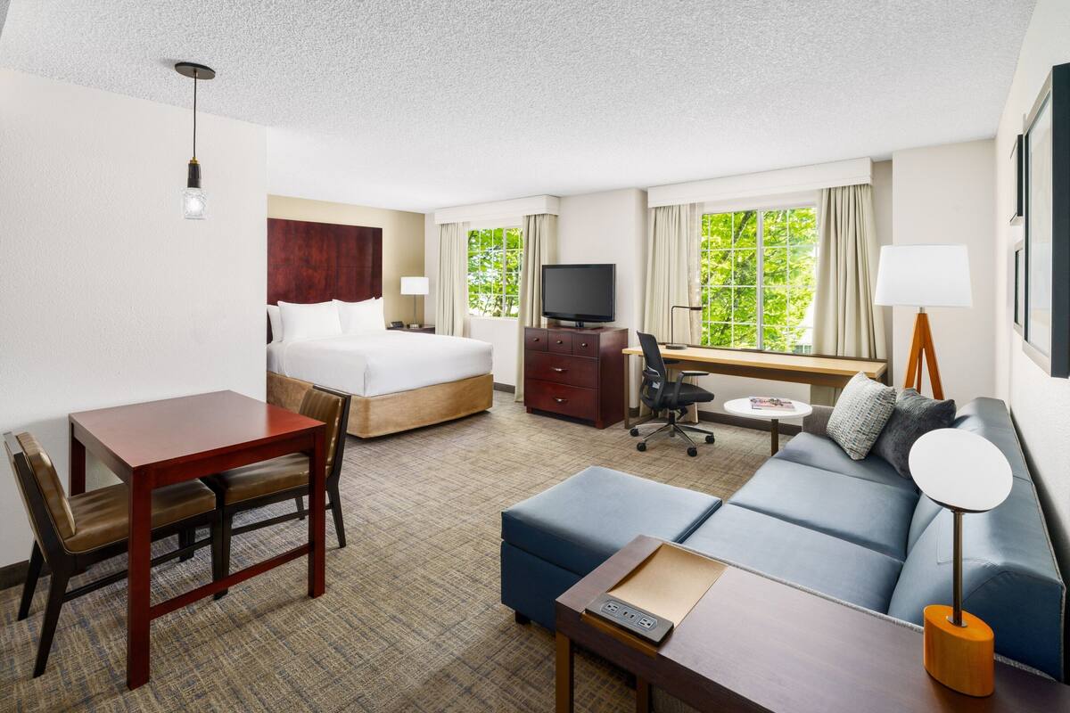 Ein Hotelzimmer mit Bett, Schreibtisch mit Stuhl, einer Couch, einem Fernseher und einer Lampe.