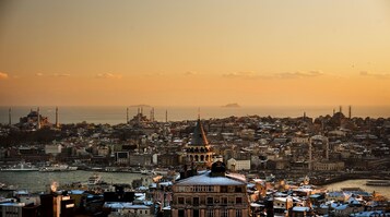 Un paisaje urbano con arquitectura histórica, incluyendo cúpulas y minaretes, y un paseo marítimo con barcos.