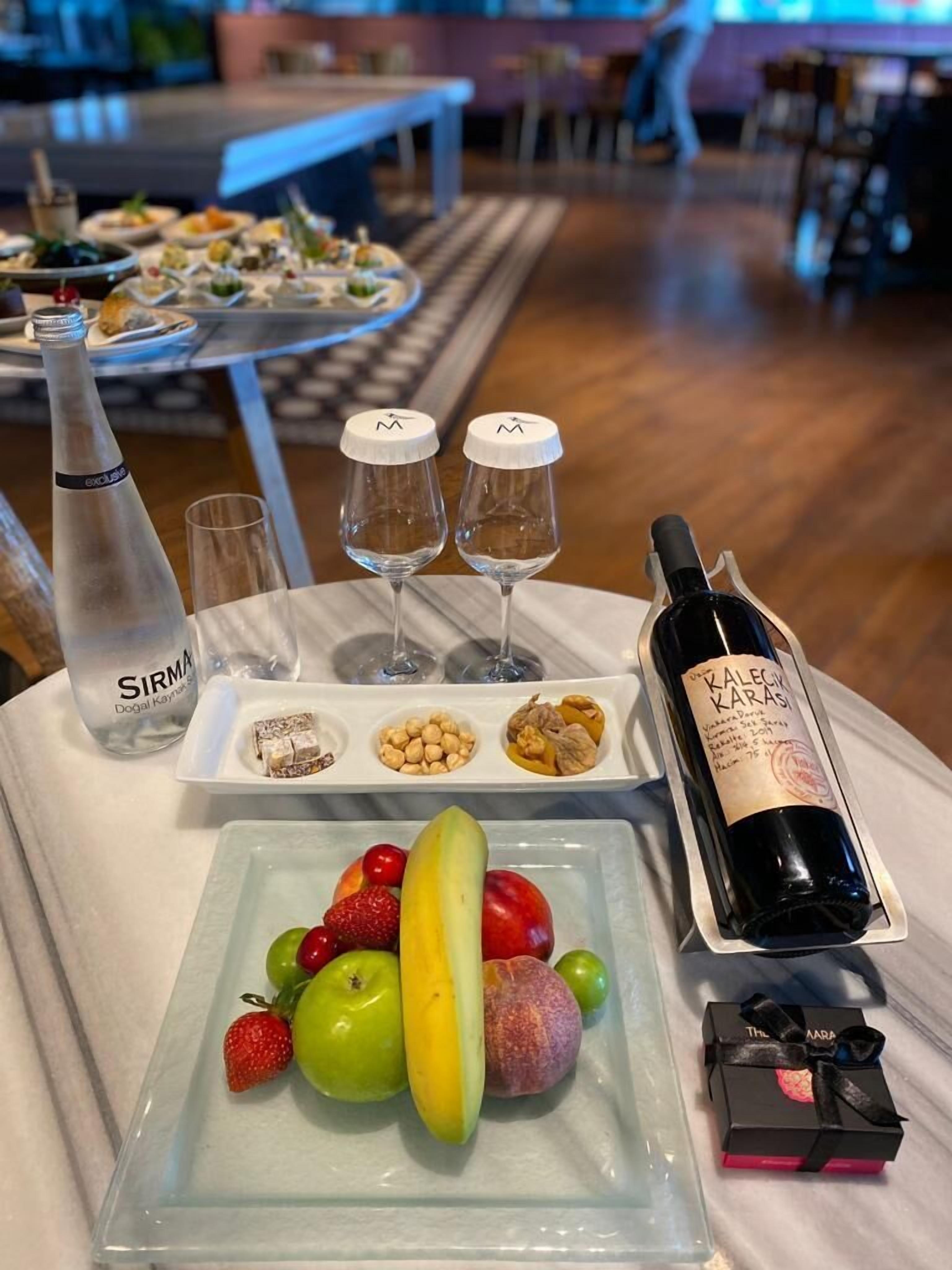 Una mesa con una botella de vino, dos copas, un plato de fruta y una botella de agua.