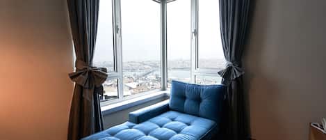 A bedroom with a large window, a bed, and curtains tied back.