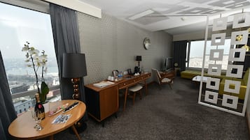 Ein Hotelzimmer mit großem Fenster, einem Schreibtisch mit Lampe, einer Couch und einem dekorativen Raumteiler.