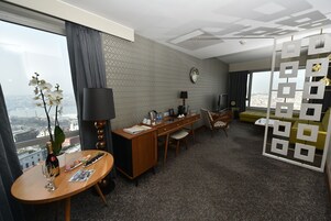 A hotel room with a large window, a desk with a lamp, a sofa, and a decorative partition.
