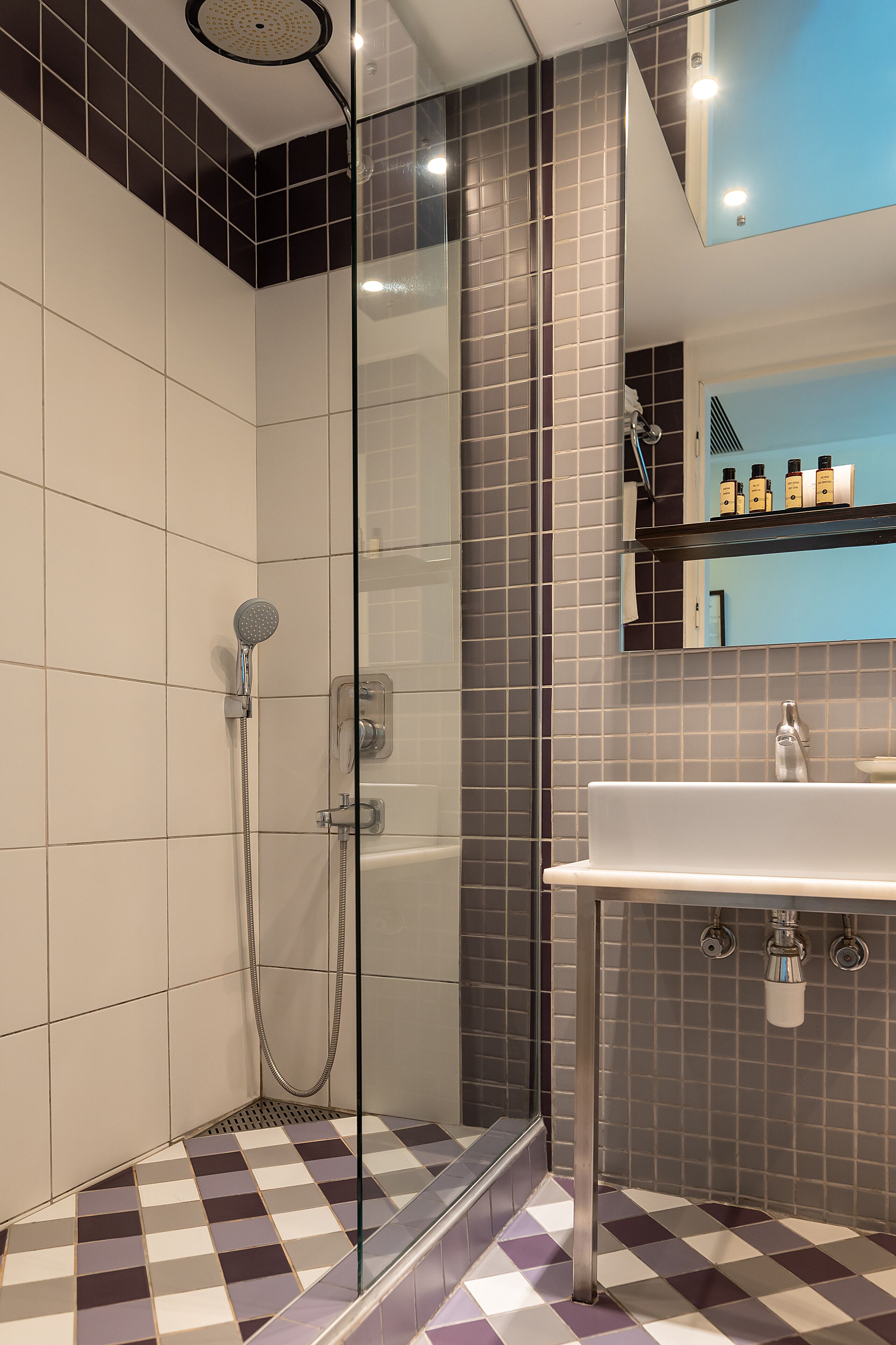 Ein modernes Badezimmer mit einer gläsernen Duschkabine, einem weißen Waschbecken und einem gefliesten Boden mit Schachbrettmuster.