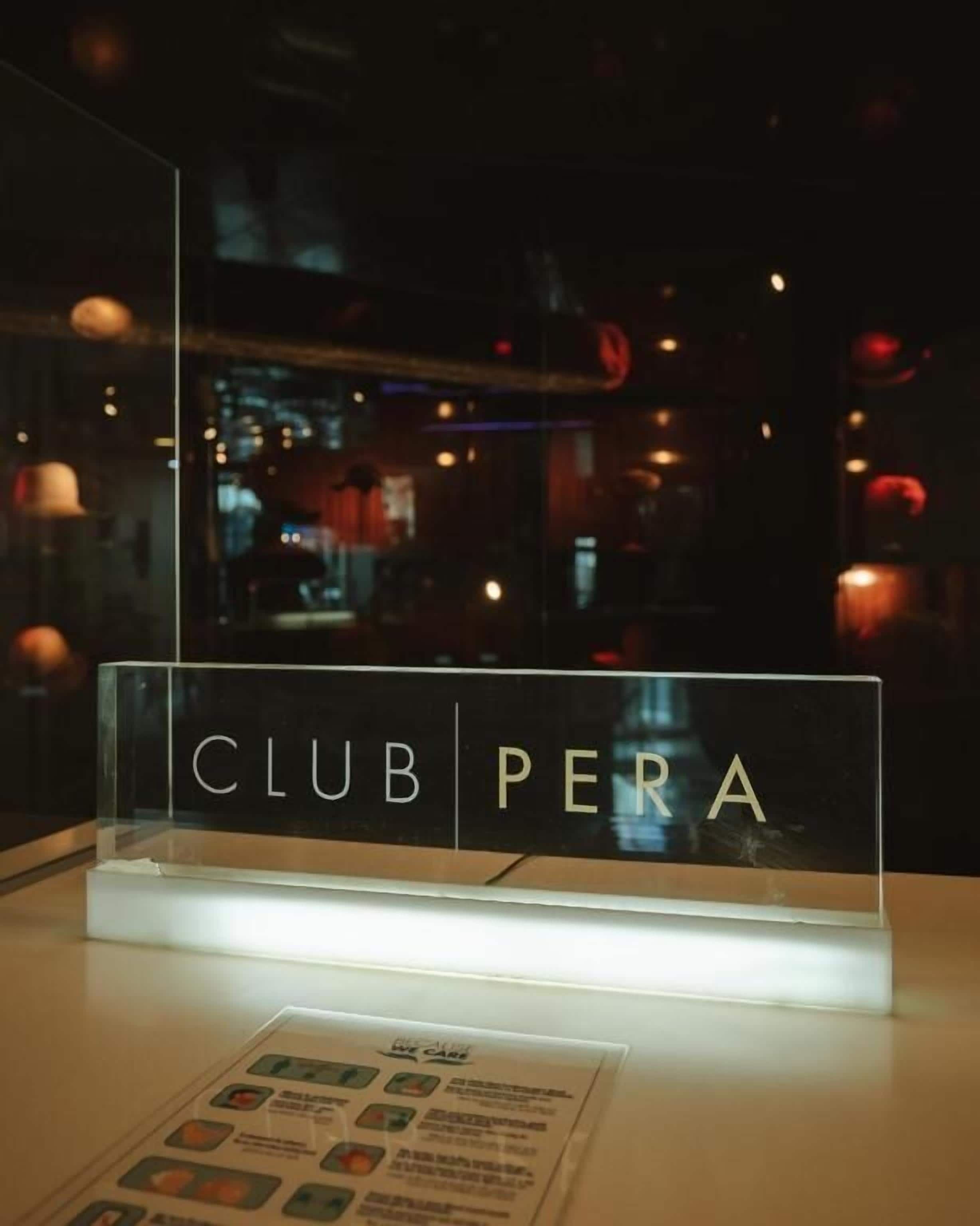 A sign with 'CLUB PERA' in a clear, illuminated display case, likely indicating a club or lounge area within a building.