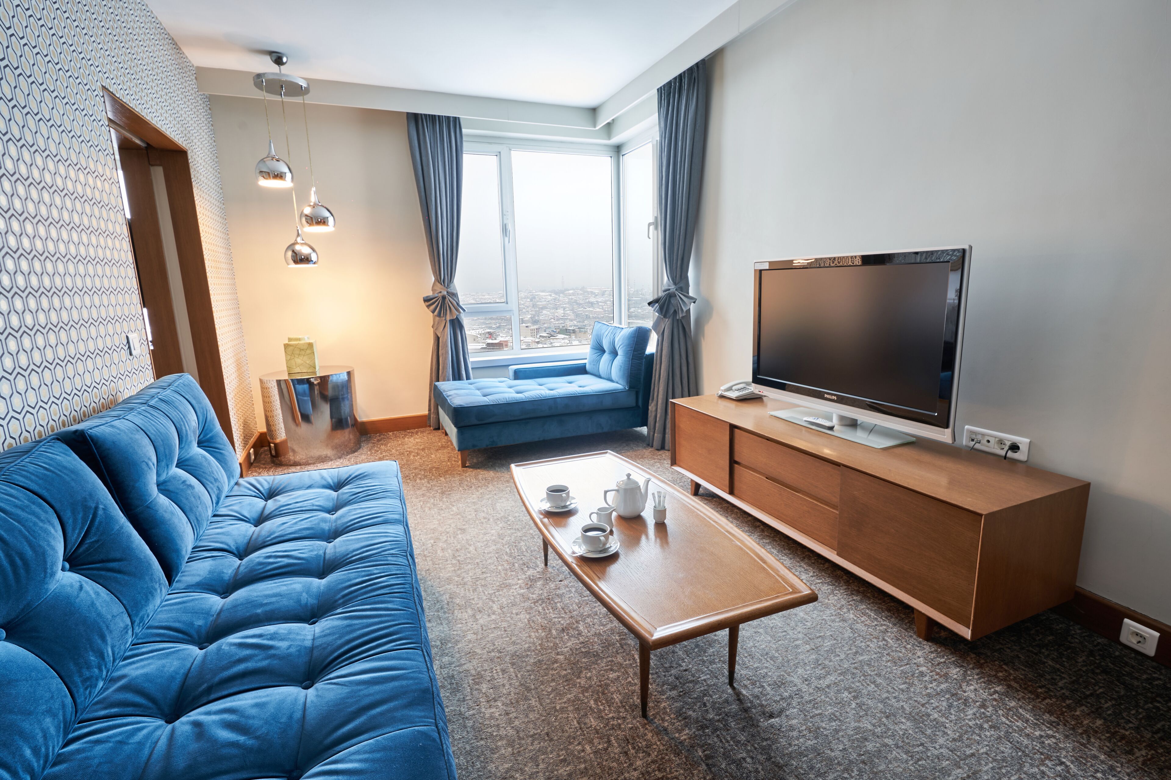 Una sala de estar moderna con un sofá azul, una mesa de centro de madera y un televisor de pantalla plana sobre un mueble de madera.
