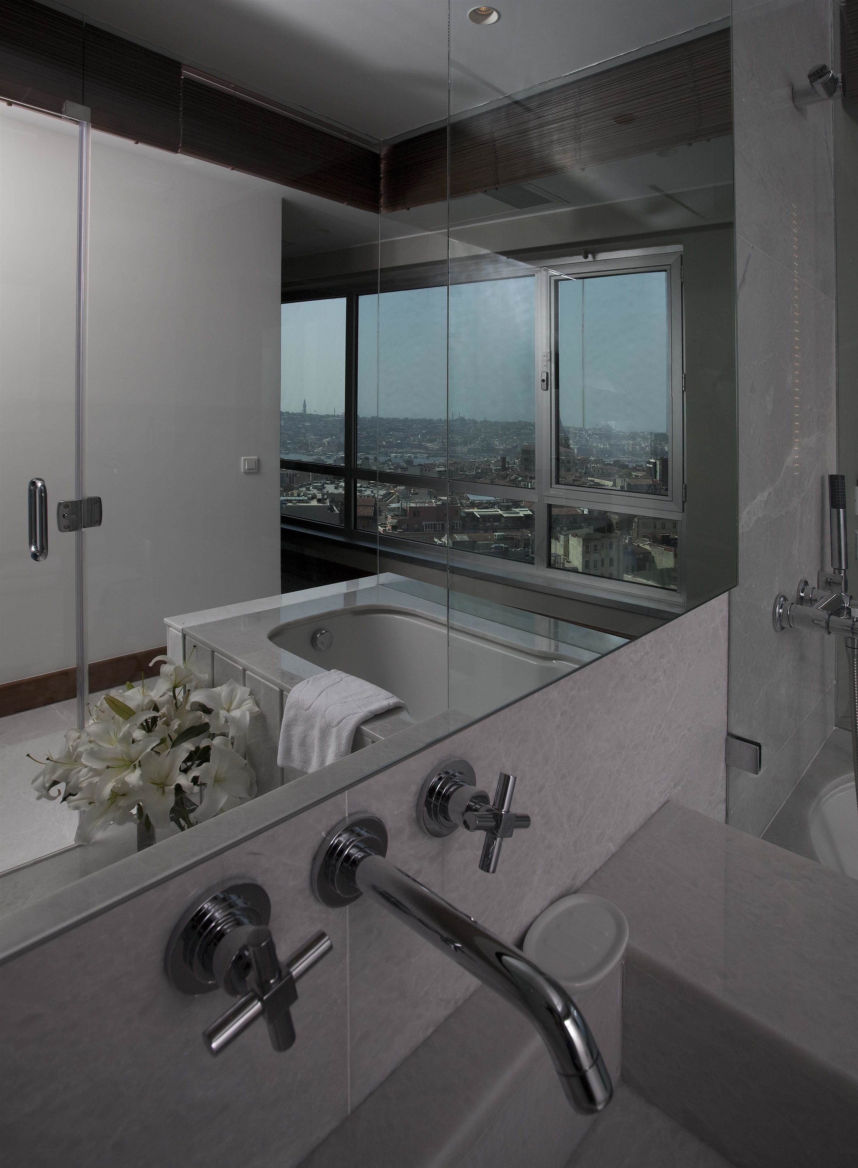 A modern bathroom with a large bathtub, a glass shower enclosure, and a view of a cityscape through large windows.