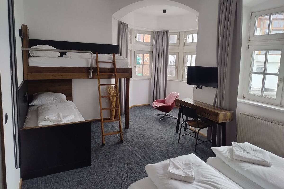 A room with bunk beds, a desk, a chair, a TV, and a window.