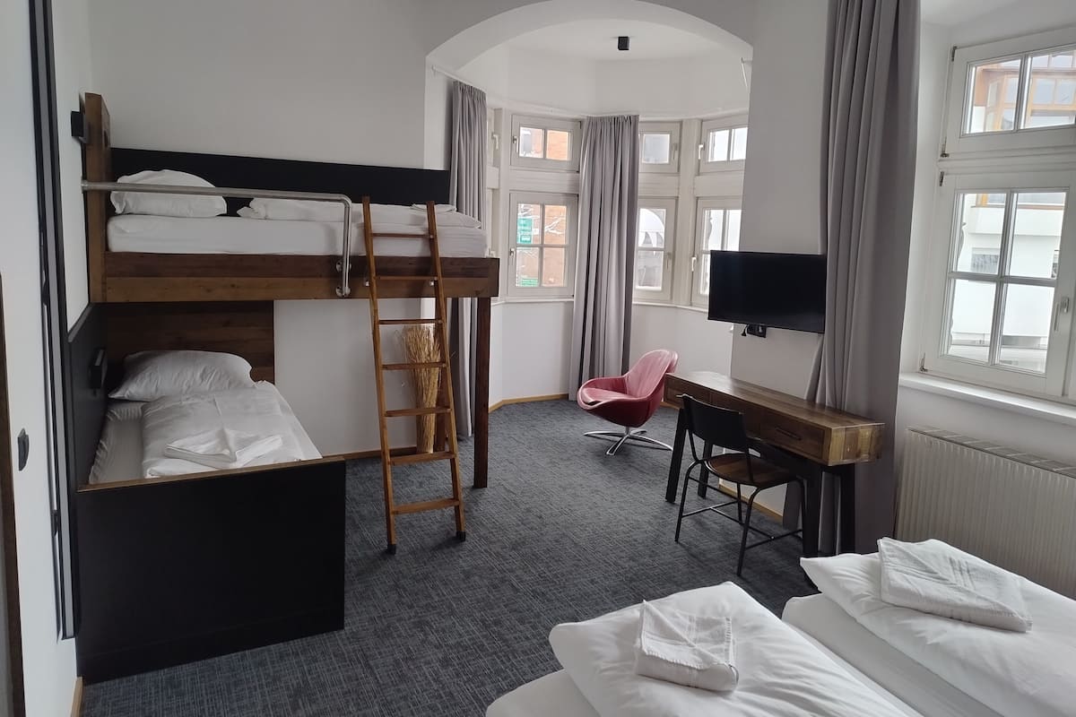 A room with bunk beds, a desk, a chair, a TV, and a window.