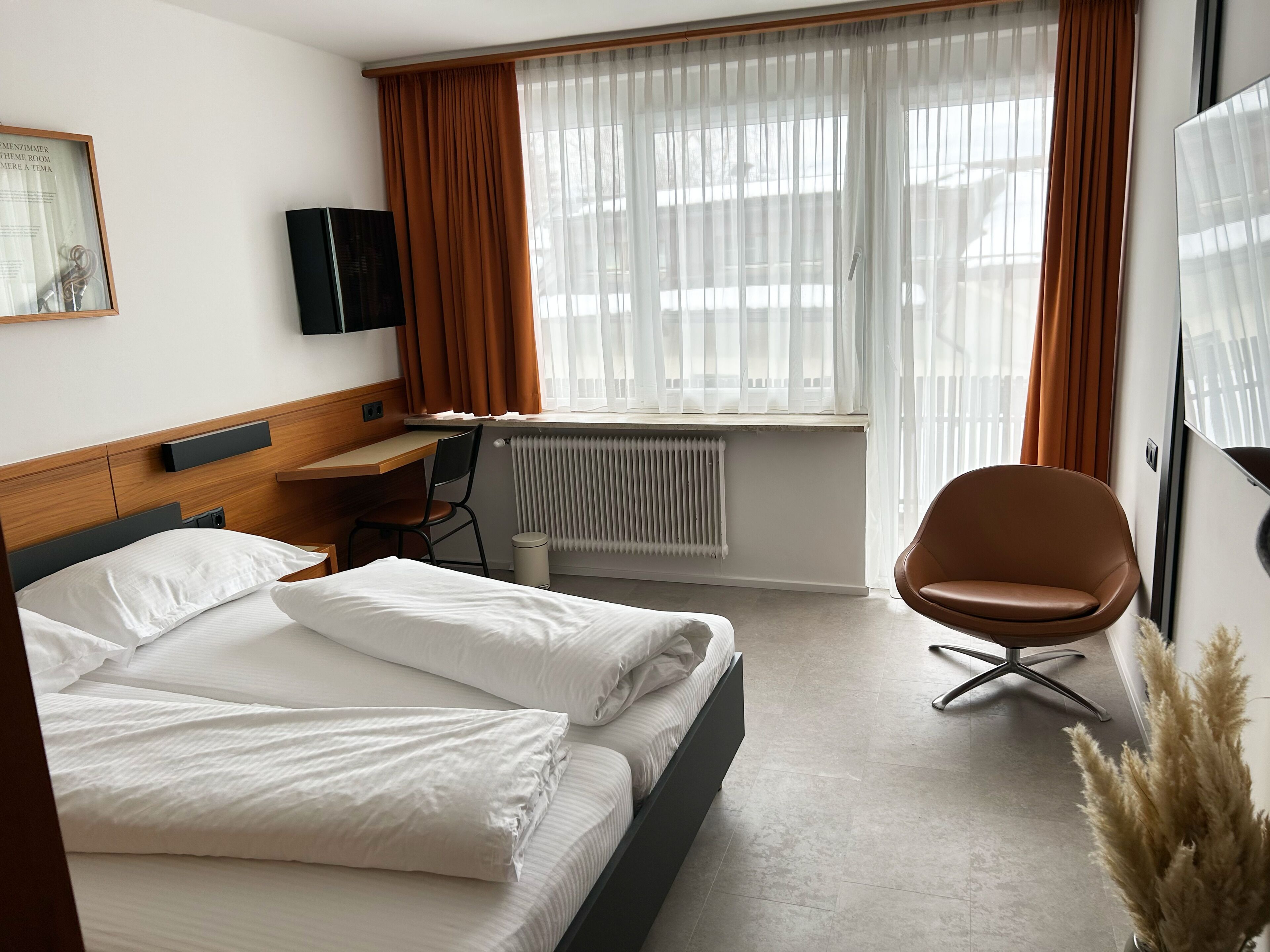 A hotel room with a bed, desk, chair, radiator, and a TV.