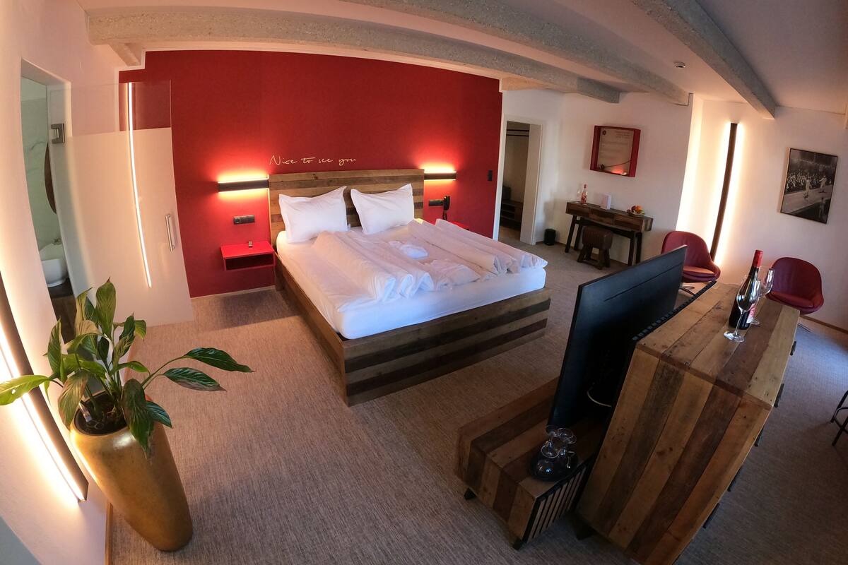 A hotel room with a bed, bedside table, desk, chairs, and a potted plant.